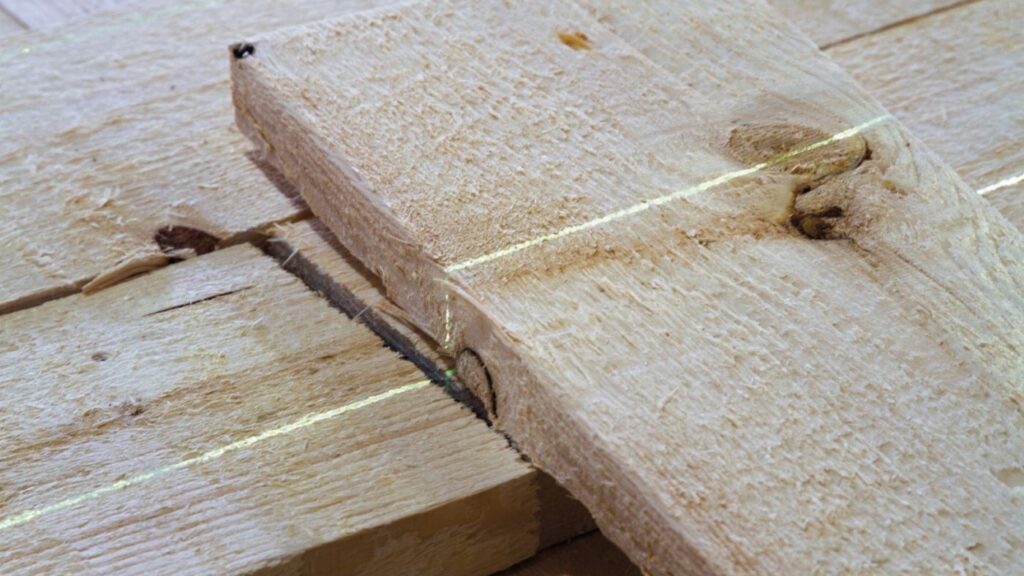 A green line laser projects a reference line onto rough-sawn timber boards to indicate the cut line for edging.