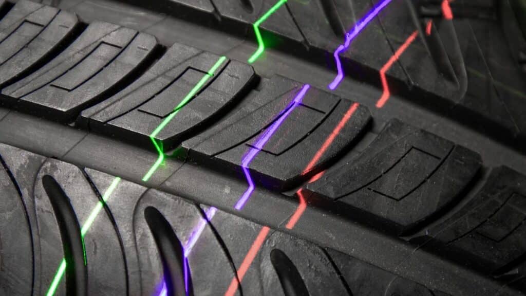 Multi-colored laser lines in red, green, and purple run across a car tire tread, serving as an optical reference for inspection and tread measurement.