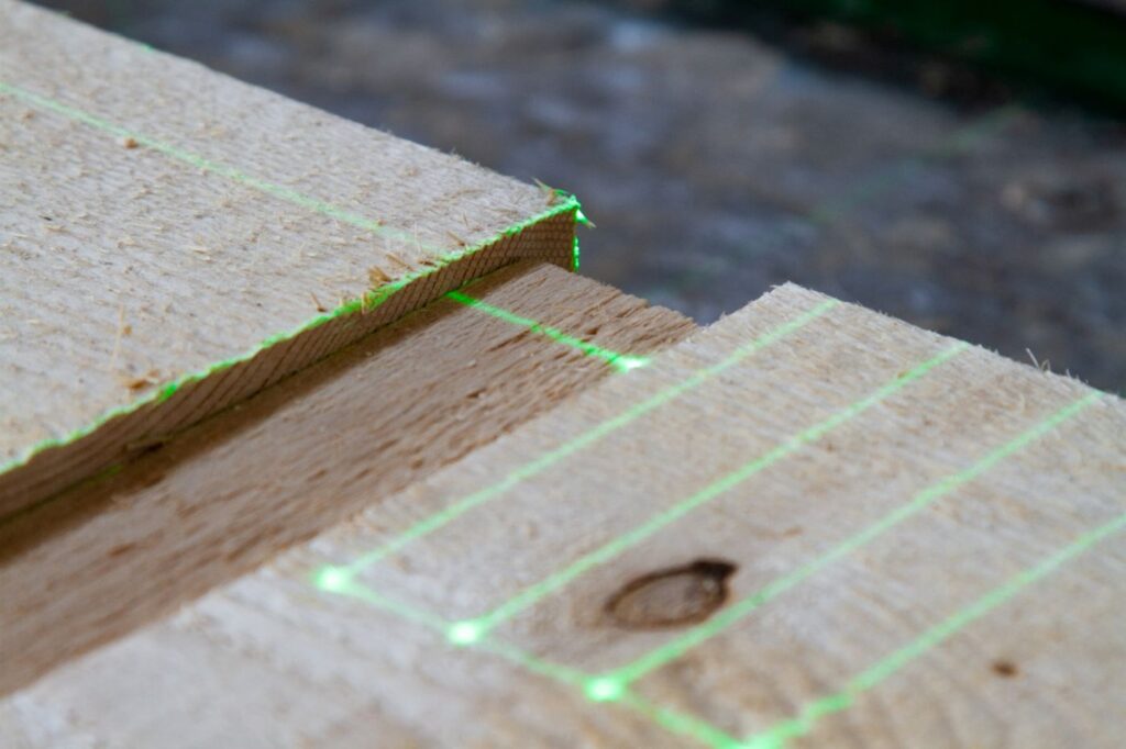 Green laser lines mark the exact placement on a timber joint during the assembly of a nail plate truss.