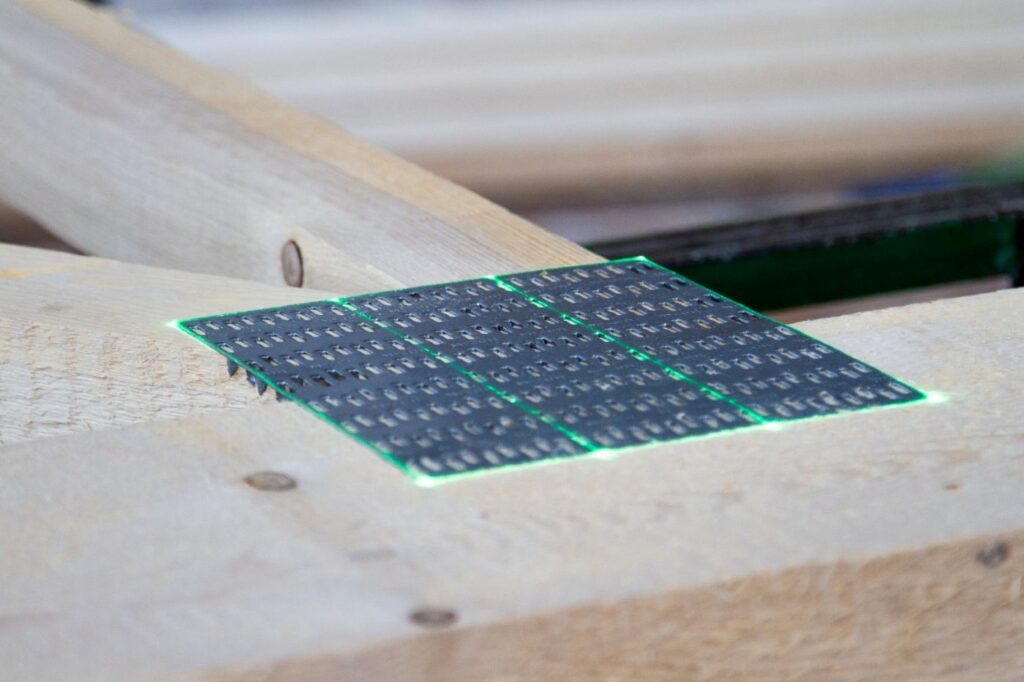 Laserporjektion markiert die exakte Position einer Nagelplatte auf einem Holzbauteil bei der Fertigung von Nageplattenbindern.