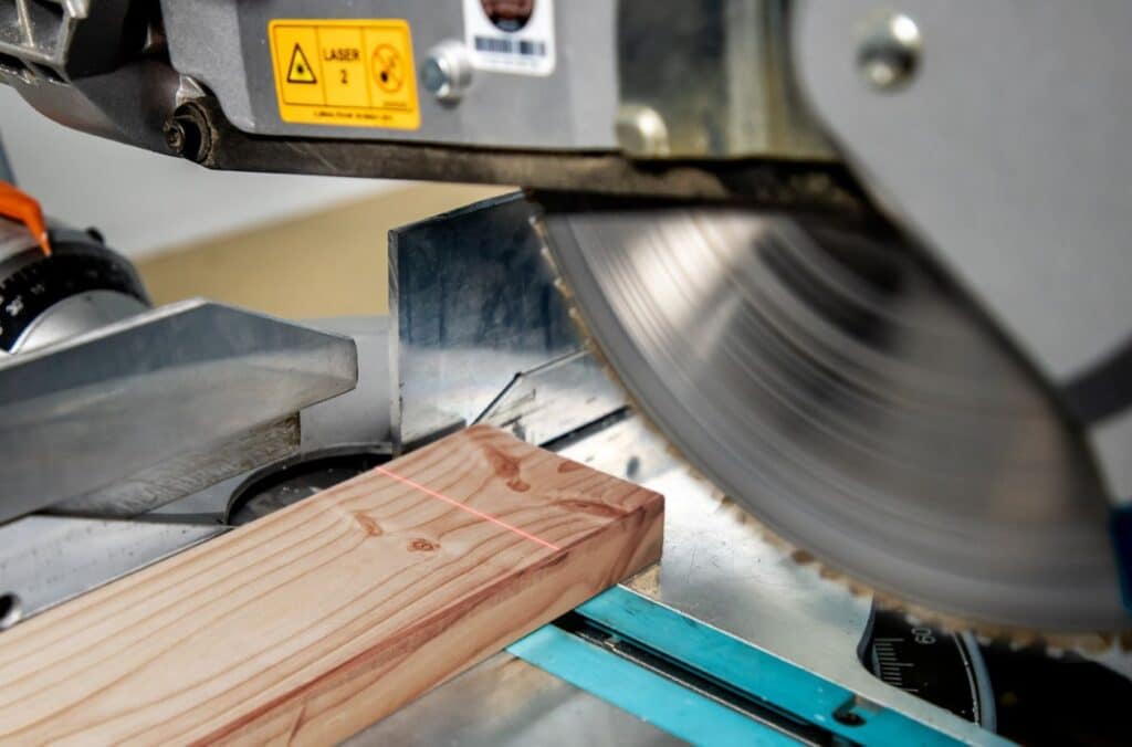 Ein roter Linienlaser projiziert die Schnittlinie auf ein Holzbrett an einer Formatkreissäge.