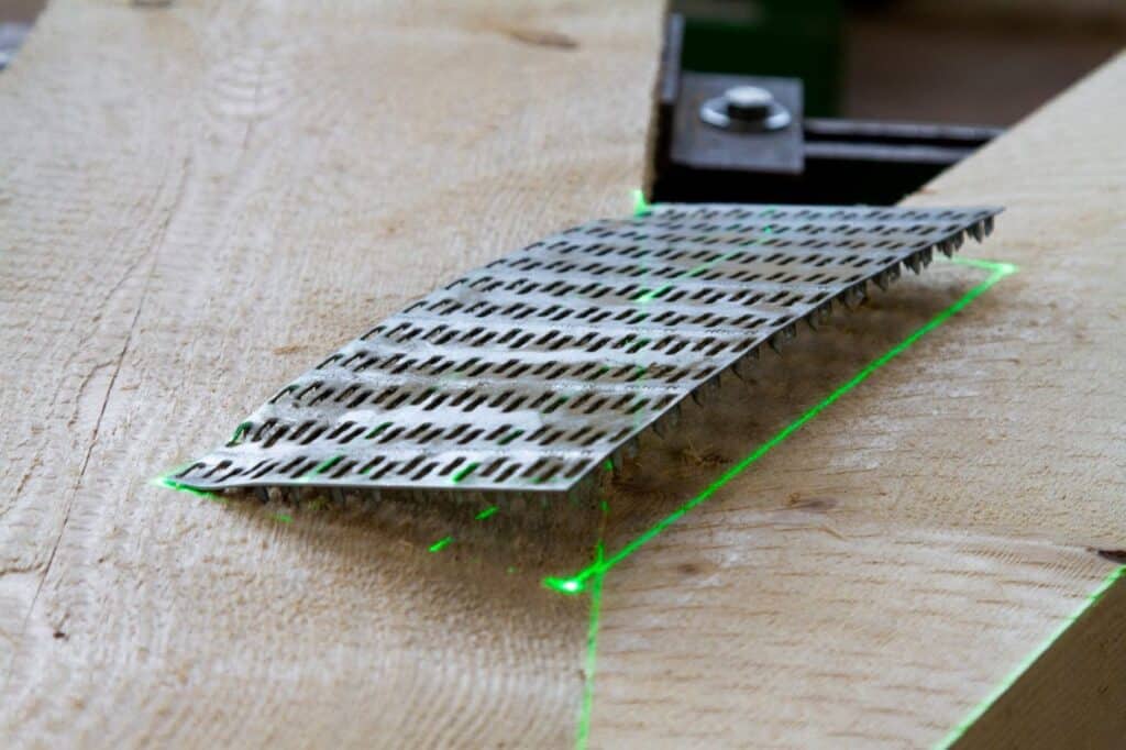 Eine grüne Laserprojektion zeigt die Soll-Platzierung einer Nagelplatte auf einem Holzträger für die Montage eines Nagelplattenbinders.