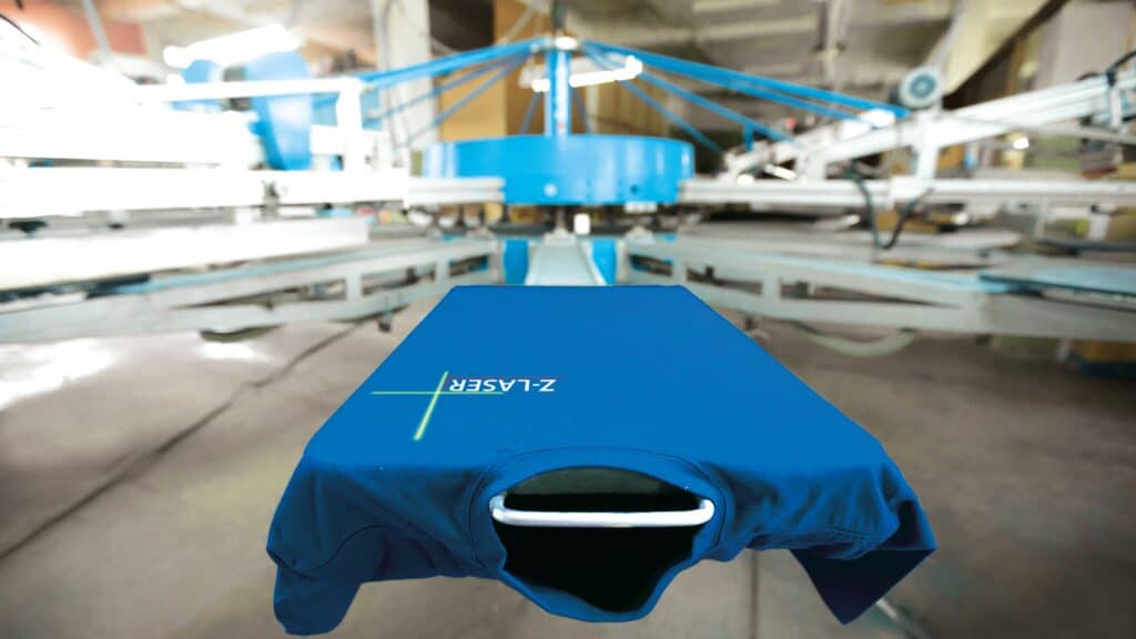A positioning laser projects a crosshair for precise alignment of a T-shirt on the pallet of a textile printing carousel.