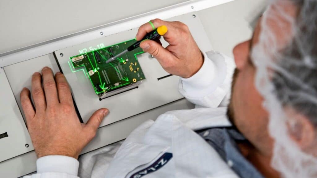 A worker assembles a PCB while a green laser projection highlights target positions and work areas for component placement.