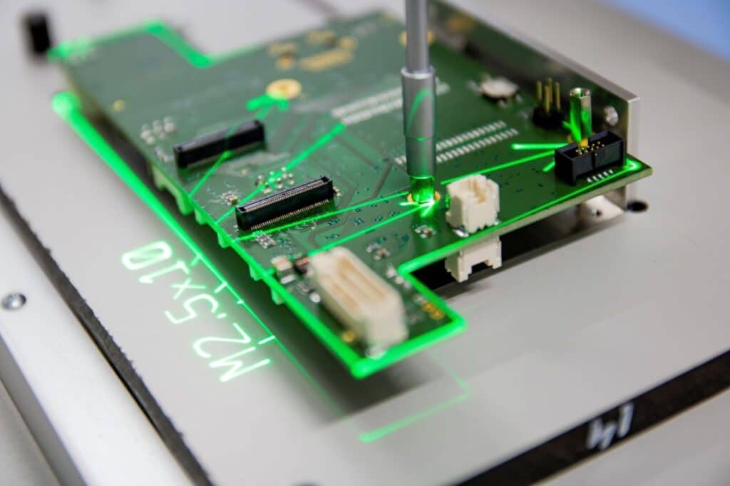 A green laser projection in a worker guidance system marks target component positions on a PCV during THT assembly.