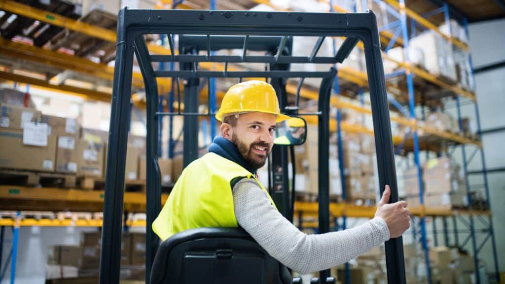 Forklift operator in warehouse operations driving between pallet racks in a high-bay storage system
