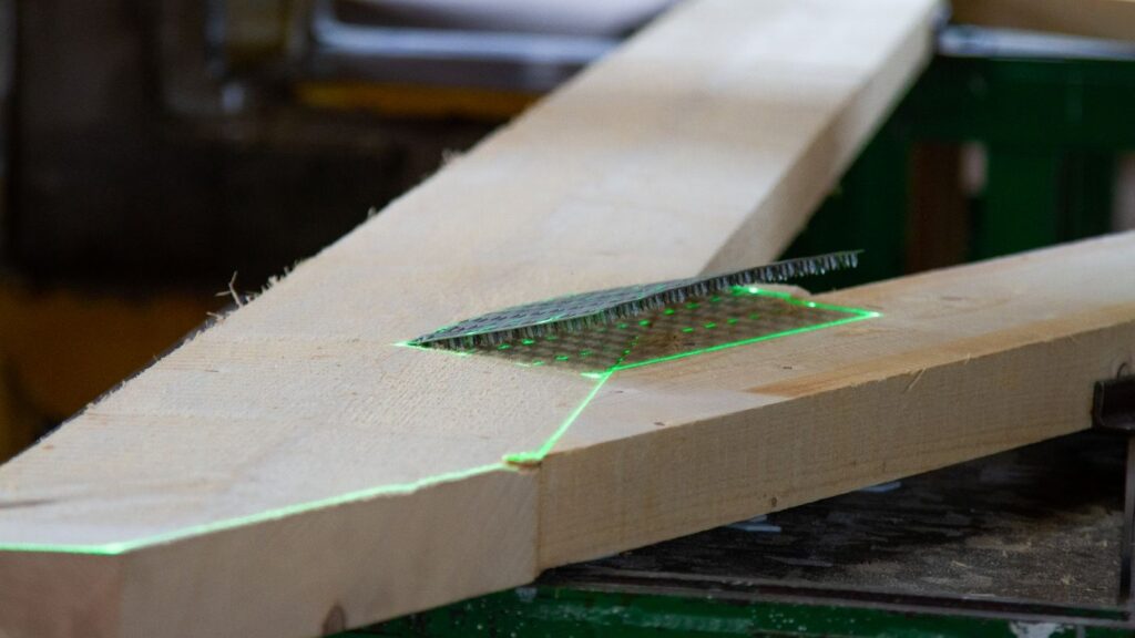Projizierte grüne Laserlinien dienen projizieren die Kontur des Nagelbinders auf Holz. Die Nagelplatte auf dem Holz wurde anhand der Laserprojektion ausgerichtet. 