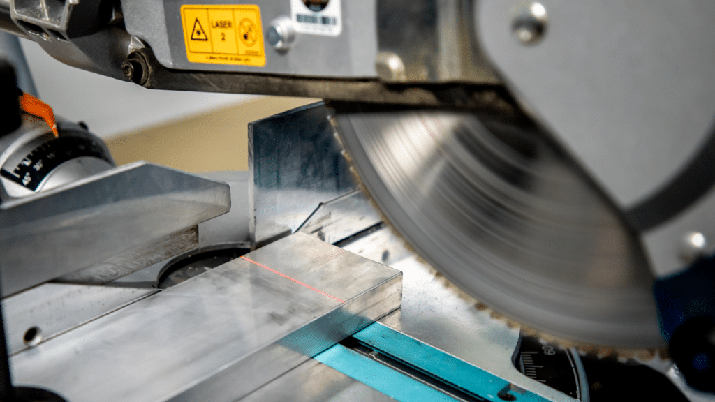 Nahaufnahme einer Metallkappsäge beim Sägen eines Aluminiumprofils; eine rote Laserlinie markiert die Schnittposition vor dem rotierenden Sägeblatt.