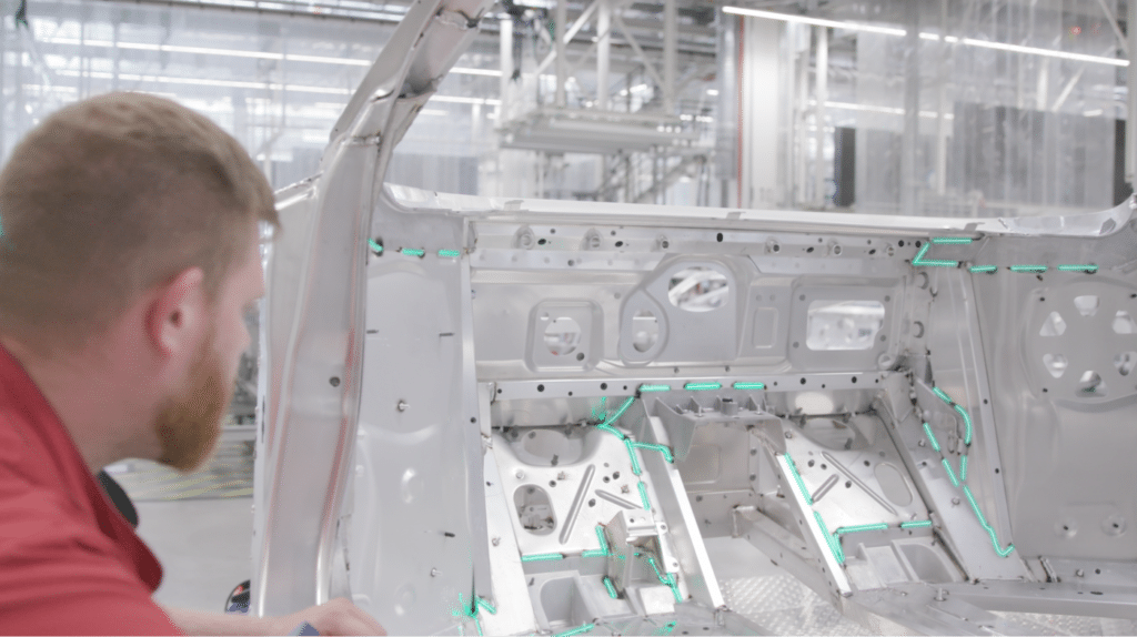 Worker inspecting the weld seam path of a body panel using green laser projection for optical surface inspection in production.