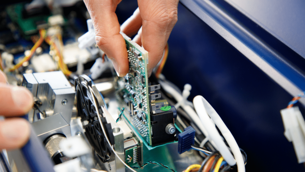 View of a hand holding a circuit board inside the opened housing of a laser projector during maintenance.